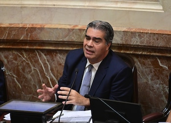 Primer plano de Jorge Capitanich, un hombre con cabello oscuro y canas, vistiendo un traje azul marino y corbata de rayas, hablando y gesticulando
