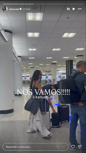 Zaira Nara camina por un aeropuerto con gafas de sol y cabello largo, arrastrando una maleta plateada. Un hombre está parcialmente visible a la derecha