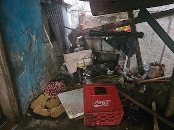 Imagen de un espacio interior deteriorado con paredes azules y grises, escombros, y una caja roja de Coca-Cola en el suelo, con el suelo cubierto de suciedad