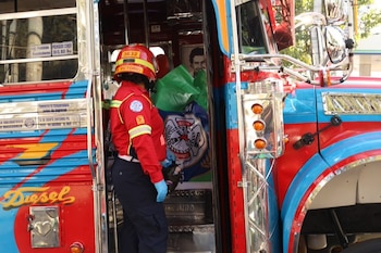 Una socorrista con casco rojo y guantes azules permanece en la puerta de un autobús decorado con pintura roja y azul