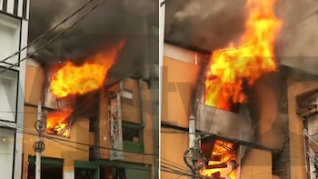 Un edificio de varios pisos en llamas, con fuego saliendo de múltiples ventanas y denso humo oscuro ascendiendo hacia el cielo