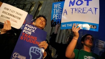 Primer plano de personas en una protesta nocturna sosteniendo pancartas con mensajes de apoyo a los derechos trans y contra la discriminación