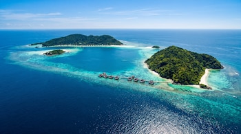 Vista aérea de islas verdes rodeadas de aguas turquesas, arrecifes de coral y una hilera de cabañas sobre el mar.