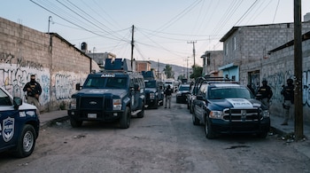 Camionetas blindadas azules de la AMIC y patrullas de la FGJES estacionadas en una calle de tierra de Nogales, Sonora, con agentes armados y muros grafitados.