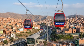 Cabinas rojas de teleférico suspendidas en cables sobre un barrio residencial de casas de ladrillo y una autopista