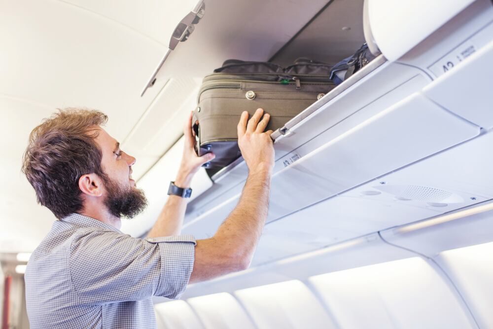Hombre metiendo una maleta en el compartimiento del avión (Shutterstock).