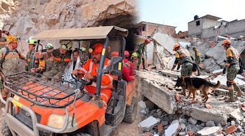 Militares y personal de rescate con un perro de búsqueda operan en un entorno rocoso con un vehículo utilitario y entre escombros de edificios colapsados.