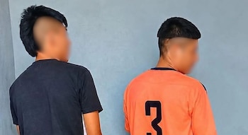 Dos jóvenes de espaldas frente a una pared, uno con camiseta negra y otro con camiseta deportiva naranja con el número tres