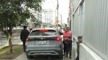 SUV Volkswagen Nivus gris con matrícula CWP-354 de Perú. Varias personas adultas y niños en acera. Calle urbana con edificios, árboles, andamios y cinta amarilla