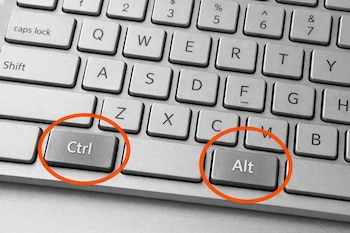 Teclado de computadora plateado con las teclas 'Ctrl' y 'Alt' claramente visibles, cada una encerrada en un círculo naranja brillante.