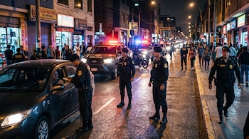 Policías con uniforme oscuro inspeccionan un vehículo y patrullan una calle de noche junto a vehículos policiales con luces encendidas.