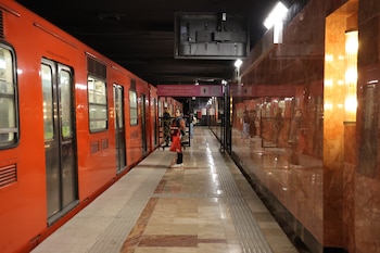 Tren de metro naranja en una estación subterránea con personas esperando en el andén, muros de mármol pulido y un cartel indicador