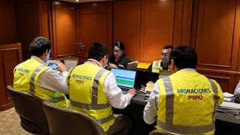 Cuatro personas con chalecos amarillos de Migraciones Perú sentadas en una mesa con laptops y documentos, realizando tareas administrativas en un interior