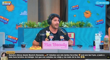 Un hombre con camiseta negra y audífonos habla ante un micrófono en un estudio de televisión decorado