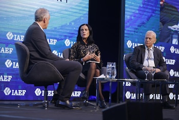 Azucena Arbeleche habla en un panel junto a German Rojas Irigoyen y otro hombre. Hay mesas de vidrio con agua y pantallas azules con el logo IAEF de fondo