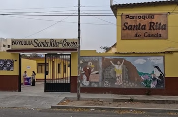 Fachada amarilla con letreros de la parroquia Santa Rita de Cascia, un mural con figuras religiosas, un portón negro y un patio interior