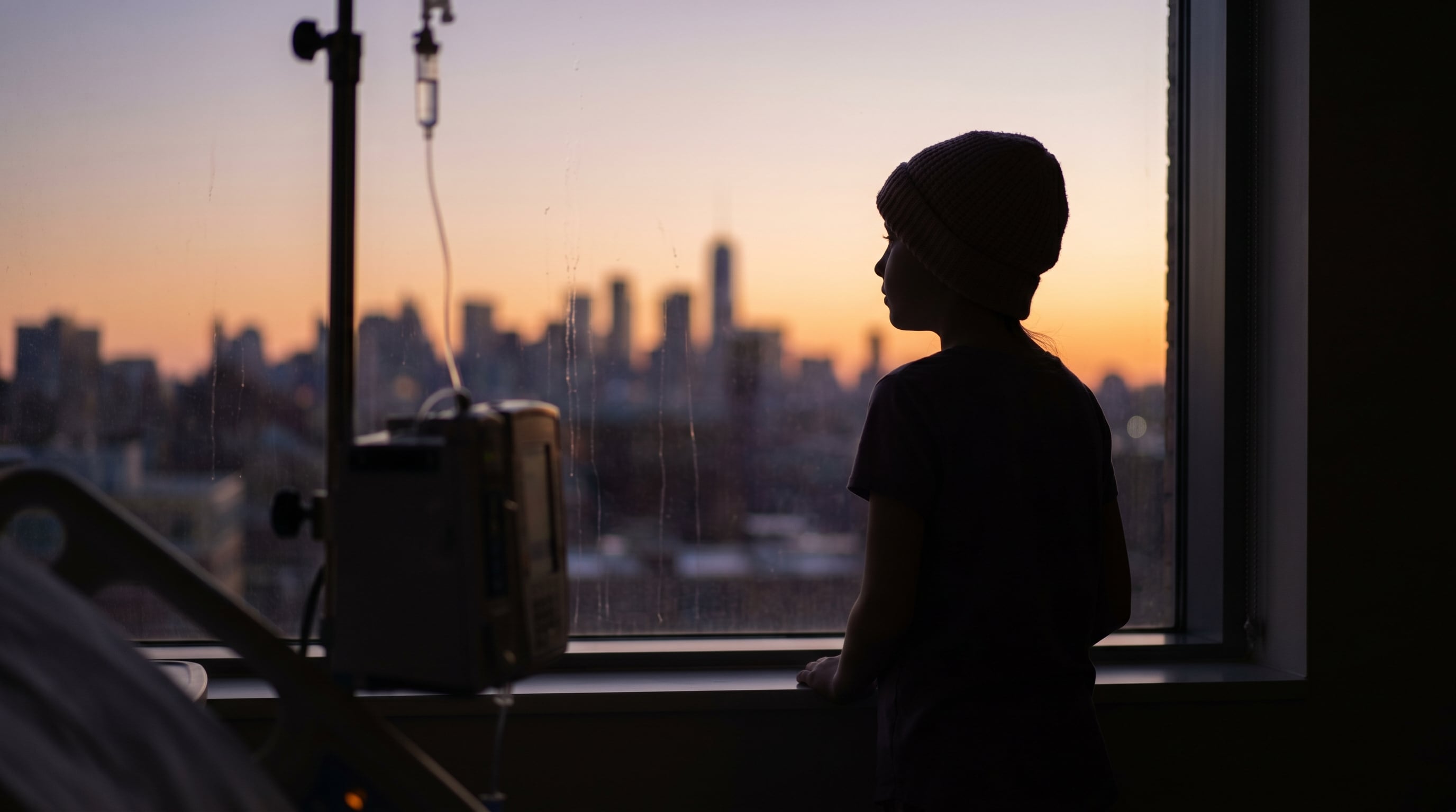 Una niña de 11 años con leucemia observa el atardecer sobre el horizonte de la ciudad desde la ventana de su habitación de hospital, mientras recibe tratamiento. (Imagen Ilustrativa Infobae)