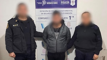 Dos agentes uniformados y una persona de civil de pie. Detrás, un cartel de la Policía de la Provincia de Buenos Aires con nombres de dependencias