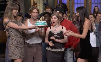 Taylor Swift sostiene un pastel celeste rodeada de personas que aplauden en un estudio de televisión
