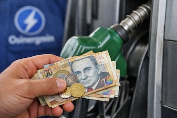 Mano sostiene billetes y monedas peruanas. Al fondo, una bomba de combustible verde y gris, y parte de un uniforme azul con el logo de Osinergmin.