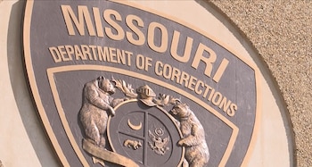 Escudo metálico con el texto en inglés Missouri Department of Corrections y relieves de osos sobre una pared