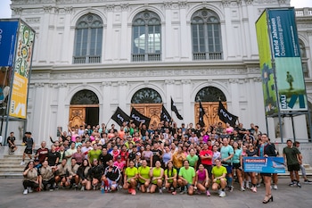 Un grupo grande de hombres y mujeres posa frente a un edificio blanco neoclásico con ventanas y columnas. Algunas personas sostienen banderas negras