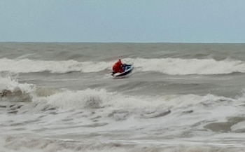 Una persona vestida de rojo navega en una moto acuática sobre la superficie del mar entre olas con espuma