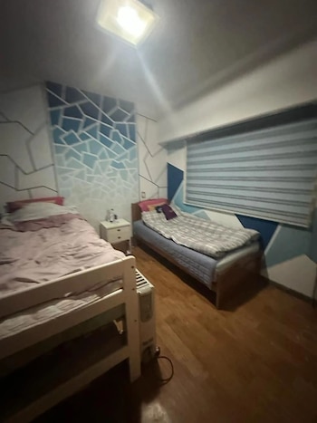 Dormitorio con dos camas individuales, paredes decoradas con patrones geométricos azules y blancos, una mesa de noche y una ventana con persianas