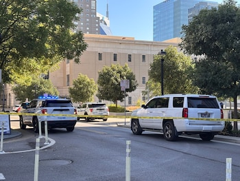 Patrullas policiales y una camioneta blanca permanecen tras una cinta amarilla de escena del crimen frente a un edificio beige en una calle urbana