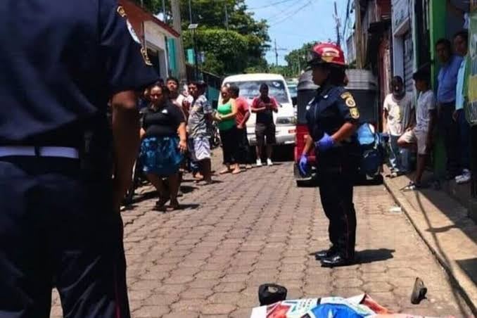 Agentes de policía resguardan una calle de San Antonio Suchitepéquez con una persona en el suelo y espectadores tras un asalto armado. (Bomberos Municipales Departamentales)