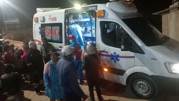 Ambulancia blanca de SAMU con luces encendidas y personal médico. Un grupo de personas, incluidos niños y adultos, se congregan cerca del vehículo en la noche