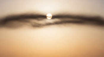Representación visual de un disco solar brillante entre una banda horizontal difusa de finas partículas suspendidas, contra un cielo con gradiente de color cálido.
