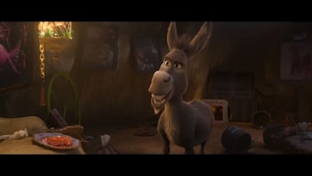 Un burro animado de pie en una habitación de piedra iluminada con luz tenue junto a un plato sobre una mesa