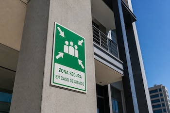 Señal verde y blanca en una columna de concreto con la frase ZONA SEGURA EN CASO DE SISMOS, flechas y siluetas humanas.