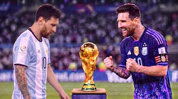 Dos representaciones de Lionel Messi con camisetas de Argentina flanquean la Copa Mundial de la FIFA sobre un pedestal en un estadio de fútbol.