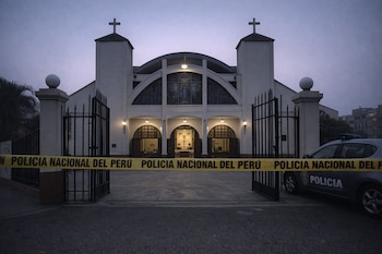 Fachada de iglesia blanca con cruces, puertas abiertas, verja negra, cinta de Policía Nacional del Perú y patrullero estacionado al amanecer.