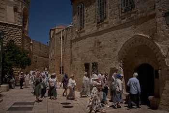 Grupo de personas caminando por una calle empedrada y estrecha, flanqueada por edificios de piedra antiguos, bajo un cielo azul brillante en Jerusalén