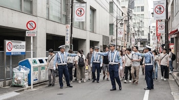 Agentes uniformados con chalecos reflectantes dirigen a peatones en una calle de Shibuya, Tokio, cerca de botes de basura y señales de 'no arrojar basura'.