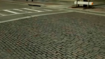 Vista aérea de una intersección con calles adoquinadas de tonos marrones y grises, junto a un paso de peatones con marcas blancas sobre asfalto oscuro