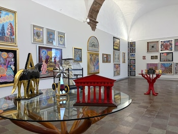 Mesa de vidrio con la maqueta roja de un templo y una figura de caballo frente a paredes blancas repletas de cuadros