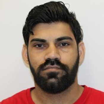 Retrato de un hombre de piel morena, cabello oscuro peinado hacia atrás y barba completa, con una camiseta roja, mirando fijamente a la cámara