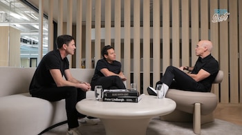 Tres hombres sentados en un sofá y una silla individual alrededor de una mesa baja, conversando en un espacio de oficina moderno con paneles de madera