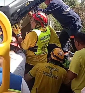 Varios socorristas con uniformes blancos y rojos inspeccionan un automóvil negro destruido junto a la estructura de un camión