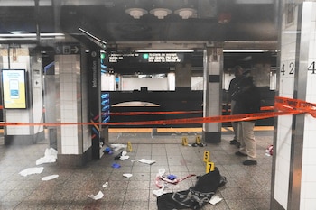 Estación de metro con cinta policial naranja, escombros, manchas de sangre y marcadores de evidencia en el andén. Dos personas al fondo
