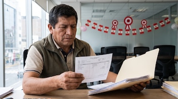 Hombre revisa un recibo de pago y documentos laborales en una oficina moderna; se observan banderas de Perú y escarapelas como decoración.