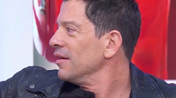 Un hombre de perfil con cabello corto y chaqueta de cuero negra en un entorno con fondo blanco y rojo.