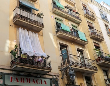 Edificio de fachada amarilla con cinco balcones de barandales de hierro forjado, ventanas, toldos verdes y azules, cortinas blancas y un cartel de farmacia