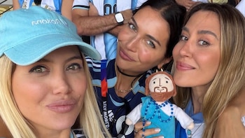 Tres mujeres en primer plano, sonrientes. Una rubia con gorra azul. Una morena con camiseta argentina y un muñeco de Jesús. Una castaña con cabello largo
