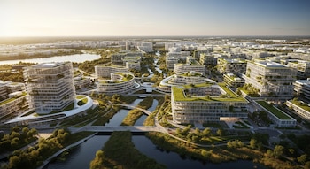 Vista aérea panorámica de una ciudad con edificios modernos de techos verdes, lagunas, ríos, senderos y puentes, todo bajo una luz cálida de atardecer.