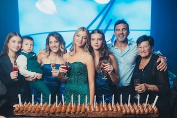Siete personas, incluyendo Allegra Cubero, su padre, Mica Viciconte, abuela y hermanos, sonríen detrás de un pastel de cumpleaños con velas en un evento familiar
